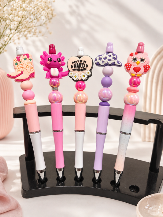 Five custom beaded pens with fun charm toppers including cowboy boots, axolotl, heart, cow print hat and strawberry owl